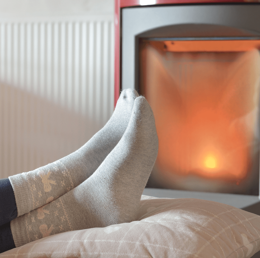 Pies con calcetines junto a estufa de gas encendida, representando el confort térmico en el hogar