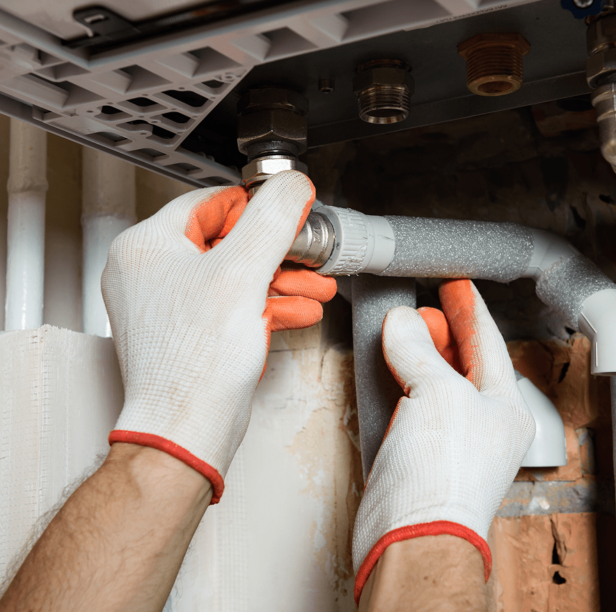 Técnico ajustando conexión hidráulica con guantes de protección en una instalación de fontanería