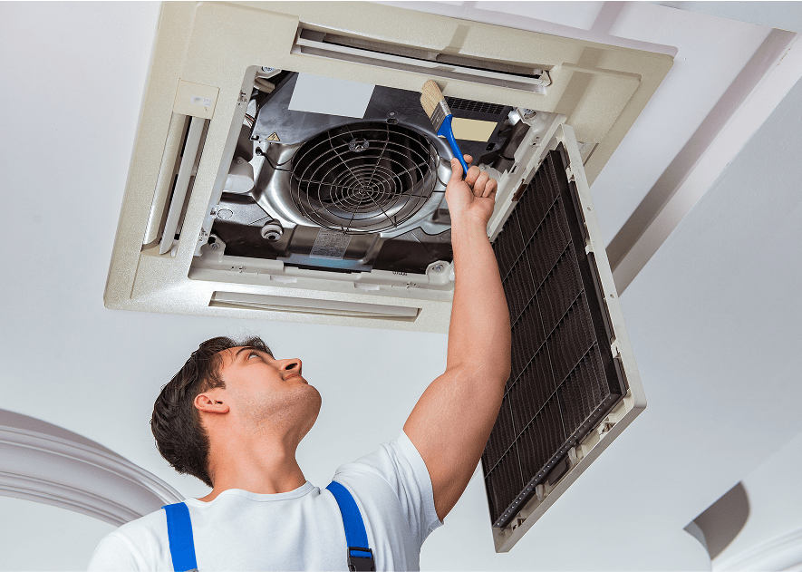 Técnico revisando y limpiando unidad de aire acondicionado instalada en el techo