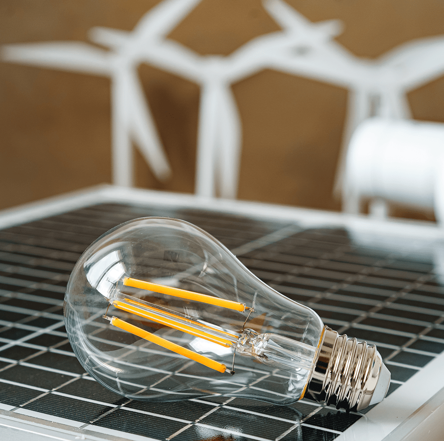 Bombilla LED sobre panel solar con aerogeneradores al fondoc